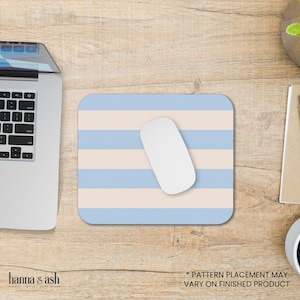Puede incluir: Una alfombrilla de ratón a rayas azules y crema con un ratón de ordenador blanco en la parte superior. El texto "* PATTERN PLACEMENT MAY VARY ON FINISHED PRODUCT" está en la parte inferior de la imagen.