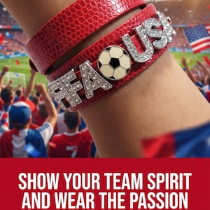 May include: A red faux leather wrap bracelet featuring silver-toned metal letters spelling FIFA USA with clear rhinestones and a central circular charm depicting a black and white football. The bracelet has a textured surface finish.