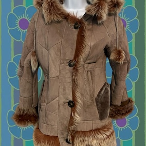 Può includere: Un cappotto vintage in pelle scamosciata marrone con cappuccio e finiture in pelliccia. Il cappotto presenta un design patchwork, grandi bottoni e inserti in pelliccia sui polsini e sull'orlo. Il cappotto è esposto su un manichino.