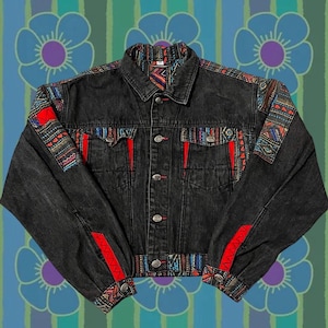Puede incluir: Una chaqueta vaquera negra con ribetes de tela estampada de colores en las mangas, el cuello y el dobladillo inferior. Los ribetes tienen acentos rojos, azules y amarillos.