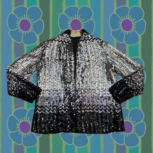 Könnte beinhalten: Vintage Paillettenjacke mit einem schwarz-silbernen Farbverlauf. Die Jacke hat lange Ärmel und einen Kragen. Der Hintergrund ist ein Blumenmuster mit blauen Blumen und grünen und blauen Streifen.