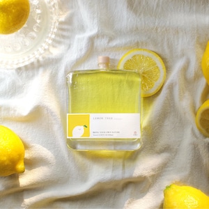 May include: A rectangular glass bottle filled with yellow liquid, featuring a label that reads LEMON TREE and BRING YOUR OWN NATURE. The bottle has a small beige cap and is surrounded by several whole yellow lemons and a single lemon slice.
