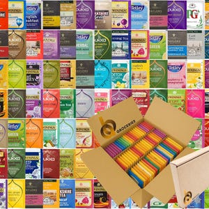 May include: A large cardboard box filled with an assortment of colourful tea bags, featuring various brands and flavours. The box is labelled with the text "BA GROCERIES" and contains rows of individually wrapped tea bags in a wide spectrum of colours.