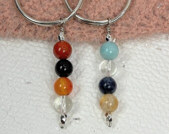 May include: Two silver keychains with a string of colorful beads. The beads are red, black, orange, clear, blue, and yellow.