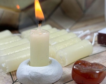 Puede incluir: Una vela blanca con una llama que arde en la parte superior de un portavelas de cerámica blanca. Hay varias otras velas blancas en el fondo, junto con un corazón de cornalina rojo.