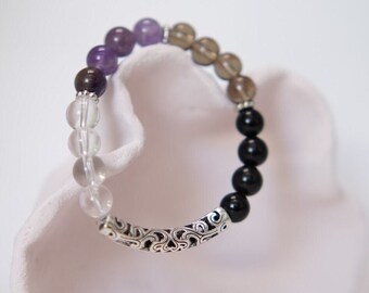 May include: A multi-coloured beaded bracelet with a silver clasp. The bracelet features amethyst, smoky quartz, clear quartz, and black onyx beads.