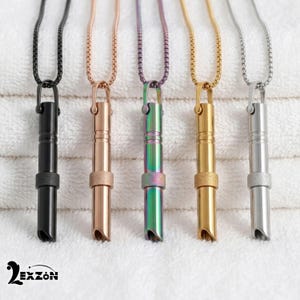 May include: Five cylindrical pendant necklaces with matching box chains, arranged in a row. The pendants come in black, rose gold, iridescent rainbow, gold, and silver finishes, each featuring a textured band and a slanted bottom opening.