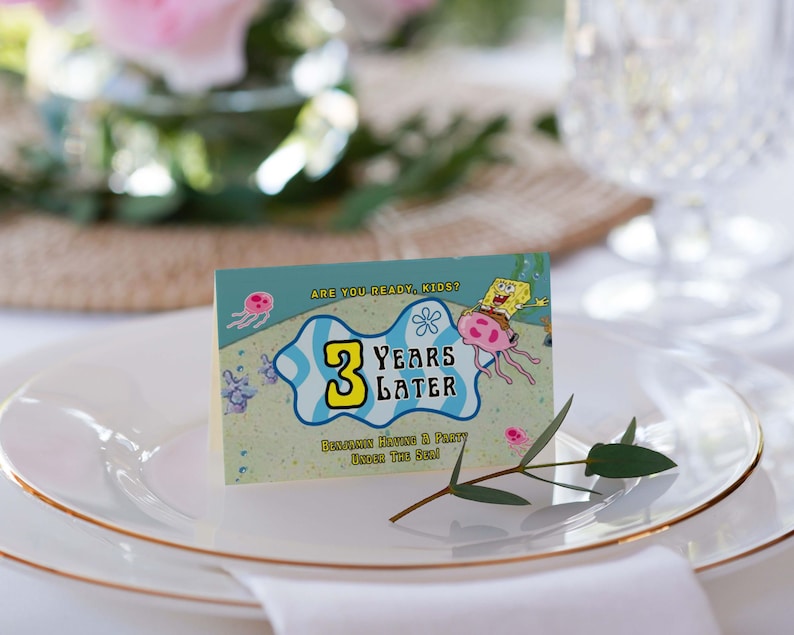 Peut inclure: Une carte de table avec une image de dessin anim&eacute; de Bob l'&eacute;ponge et une m&eacute;duse. Le texte sur la carte dit "&Ecirc;tes-vous pr&ecirc;ts, les enfants ? 3 ans plus tard. Benjamin organise une f&ecirc;te sous la mer !"