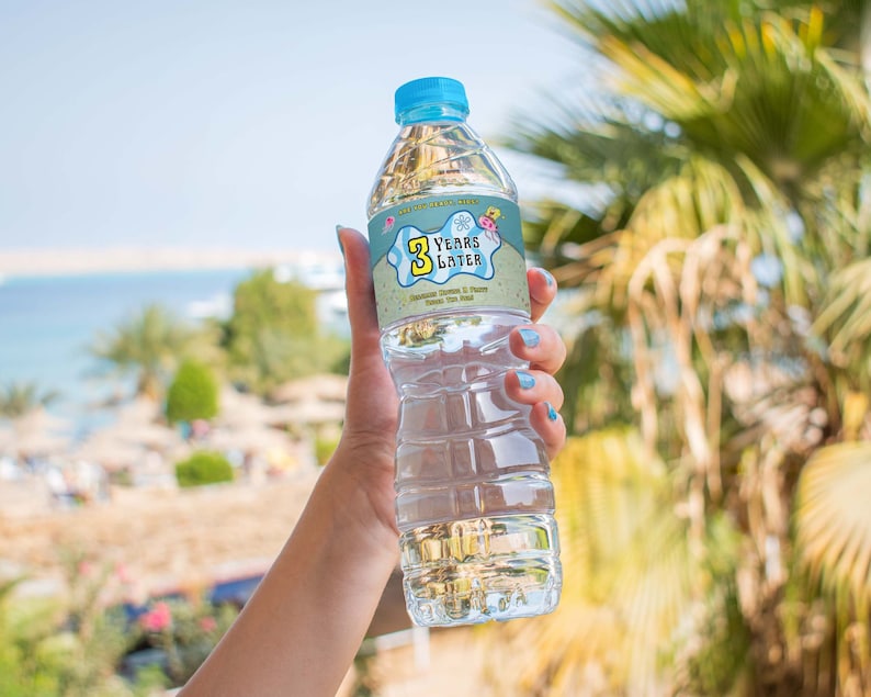 Peut inclure: Une bouteille d'eau en plastique transparente avec une &eacute;tiquette bleue et jaune qui dit "3 Years Later". L'&eacute;tiquette a un design de dessin anim&eacute; avec une &eacute;toile de mer, une coquille et un crabe.