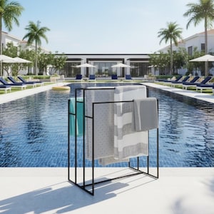 May include: A black metal towel rack holding several towels of different colors and patterns. The towels include a teal, a gray with white polka dots, a gray and white striped, and a solid gray towel. The rack is near a swimming pool.