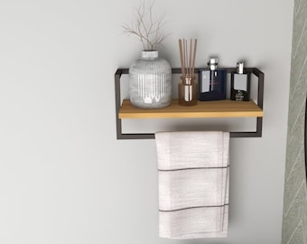 May include: A black metal shelf with a wooden top, a towel bar, and a white towel hanging on it. There are two bottles of perfume and a vase with dried flowers on the shelf. The shelf is mounted on a white wall.
