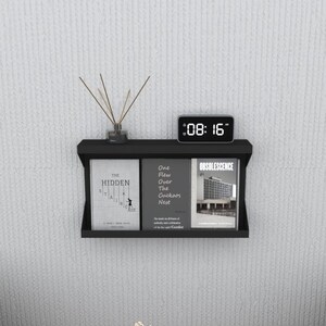 May include: Black wall shelf with two books and a digital clock. The books are titled "The Hidden" and "One Flew Over The Cuckoo's Nest". The clock displays the time 08:16.