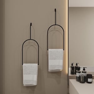 May include: Two black metal towel racks with arched tops, each holding a white towel. The racks are mounted on a beige wall.