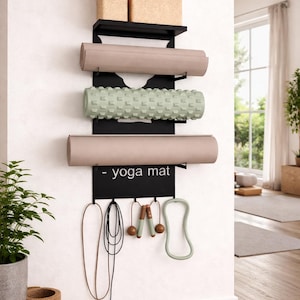 May include: Black metal yoga mat and equipment organiser mounted on a white wall. It holds rolled yoga mats, foam rollers, yoga blocks, jump ropes, and a resistance band. The text "- yoga mat" is displayed on the organiser.