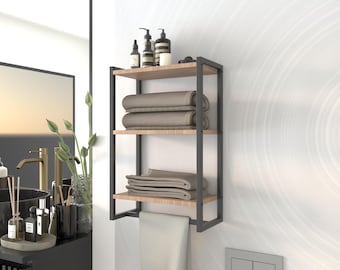 May include: A black metal bathroom shelf with three wooden shelves. The shelf is mounted on a white wall and has towels and toiletries on it.