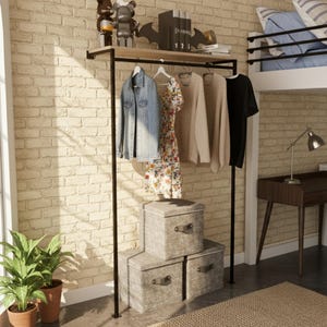 Pode incluir: Um cabideiro de metal preto com uma prateleira de madeira e roupas penduradas. Uma jaqueta jeans, um vestido floral e suéteres penduram no cabideiro. Três caixas de armazenamento cinzentas estão abaixo. O fundo é uma parede de tijolos.