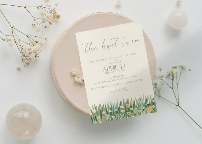 K&ouml;nnte beinhalten: Eine wei&szlig;e Karte mit gr&uuml;nem Gras und Blumen am unteren Rand. Der Text auf der Karte lautet "The hunt is on" und "Join us for Easter lunch and an egg hunt Sunday April 12 Three o'clock PM.  Come hungry!  Bring your Easter basket & a dish to share.  Hop to it!"