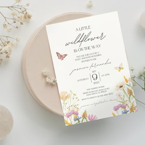 Puede incluir: Una invitaci&oacute;n de baby shower blanca con un borde floral y mariposas. El texto dice "A Little Wildflower is on the Way" e incluye el nombre "Jasmine Fernandes", la fecha "9 de septiembre de 2023" y la hora "4 PM".