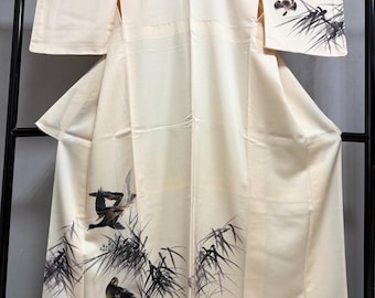 May include: Cream-colored kimono with a detailed illustration of birds and bamboo. The artwork is rendered in black and gray ink, creating a striking contrast against the soft background. The kimono is displayed on a black rack.