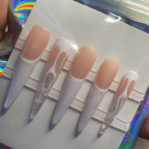 May include: Set of six long, white, fake nails with a clear, glittery base. Some nails have a white drip design.