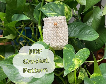 May include: A crocheted drawstring bag in a cream color with a wooden bead accent. The bag is hanging from a green leafy plant. The text "PDF Crochet Pattern" is written in a white cloud shape.