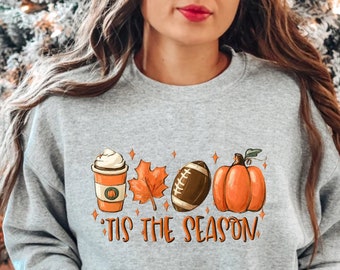 May include: A gray sweatshirt with a graphic design of a coffee cup, a football, a pumpkin, and fall leaves. The text "'Tis the season" is printed below the graphic.