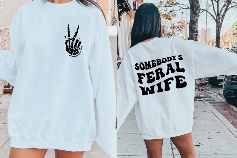 May include: White sweatshirt with a black skeleton hand making a peace sign on the front and the text "Somebody's Feral Wife" on the back.