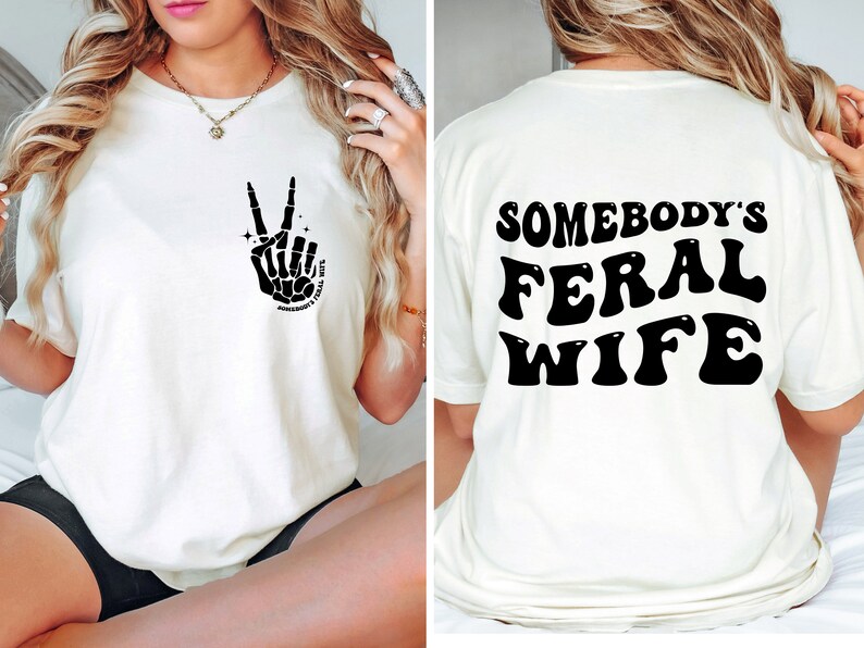 May include: White t-shirt with a black skeleton hand making a peace sign on the front and the text "Somebody's Feral Wife" in black on the back.