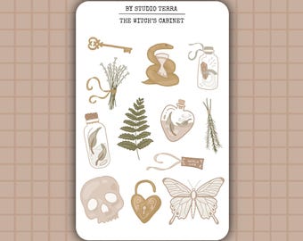 May include: A sticker sheet featuring illustrations of witchy items in beige and brown tones. Includes a key, snake, hourglass, bottles, skull, fern, butterfly, and a heart-shaped lock. The text "BY STUDIO TERRA" and "THE WITCH'S CABINET" are at the top.