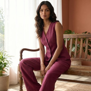 May include: A deep berry-colored sleeveless vest with a V-neckline and a front button closure, paired with matching wide-leg trousers. The set is crafted from a textured fabric and features a tailored fit with a clean, minimalist silhouette.