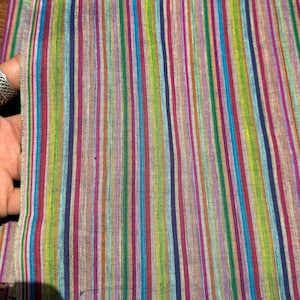 Może przedstawiać: Kolorowa tkanina z pionowymi paskami w różnych kolorach, w tym zielonym, niebieskim, różowym i fioletowym. Tkanina jest złożona, ukazując swoją fakturę i wzór. Zdjęcie przedstawia zbliżenie na tkaninę, podkreślając żywe kolory i design.