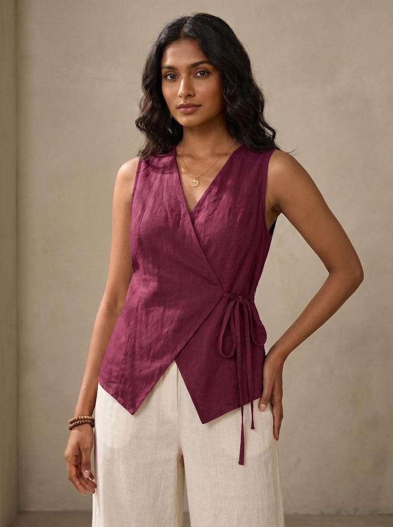 A woman wearing a purple sleeveless top with a tie at the waist, posing against a beige background.