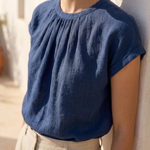 Peut inclure: Un haut en lin bleu marine avec un col fronc&eacute; et des manches courtes &agrave; revers. Le haut est fait d'un tissu doux et textur&eacute; et a une coupe d&eacute;contract&eacute;e. Le mod&egrave;le porte le haut avec un pantalon beige.