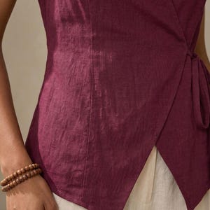 A close-up view of a person wearing a burgundy top and white pants, with a bracelet on their wrist.