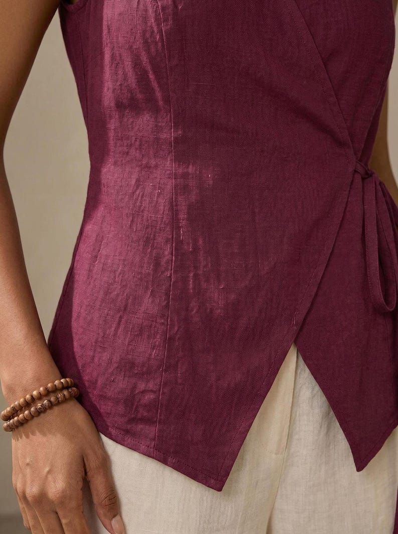 A close-up view of a person wearing a burgundy top and white pants, with a bracelet on their wrist.