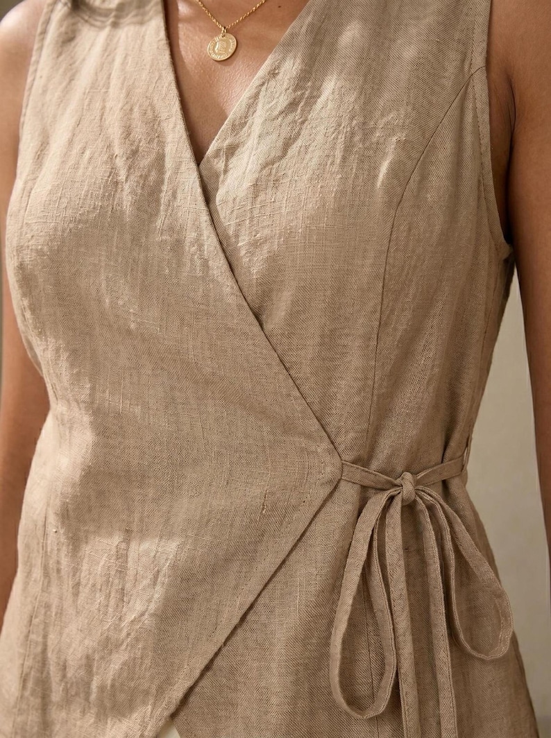A close-up view of a beige dress with a tie at the waist, featuring a gold necklace.