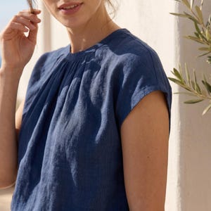 Peut inclure: Gros plan sur un haut en lin bleu avec un col fronc&eacute; et des manches courtes. Le haut a un design simple et &eacute;l&eacute;gant et est fait d'un tissu doux et textur&eacute;. Le haut est de couleur unie et semble l&eacute;ger.