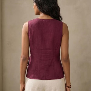 A woman wearing a maroon sleeveless top and white pants is facing away from the camera, with her back to the viewer.