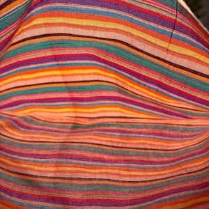 May include: Close-up of a colorful fabric with horizontal stripes in various colors, including red, orange, yellow, green, purple, and blue. The fabric appears to be woven, with a slightly textured surface. The stripes vary in width, creating a dynamic pattern.