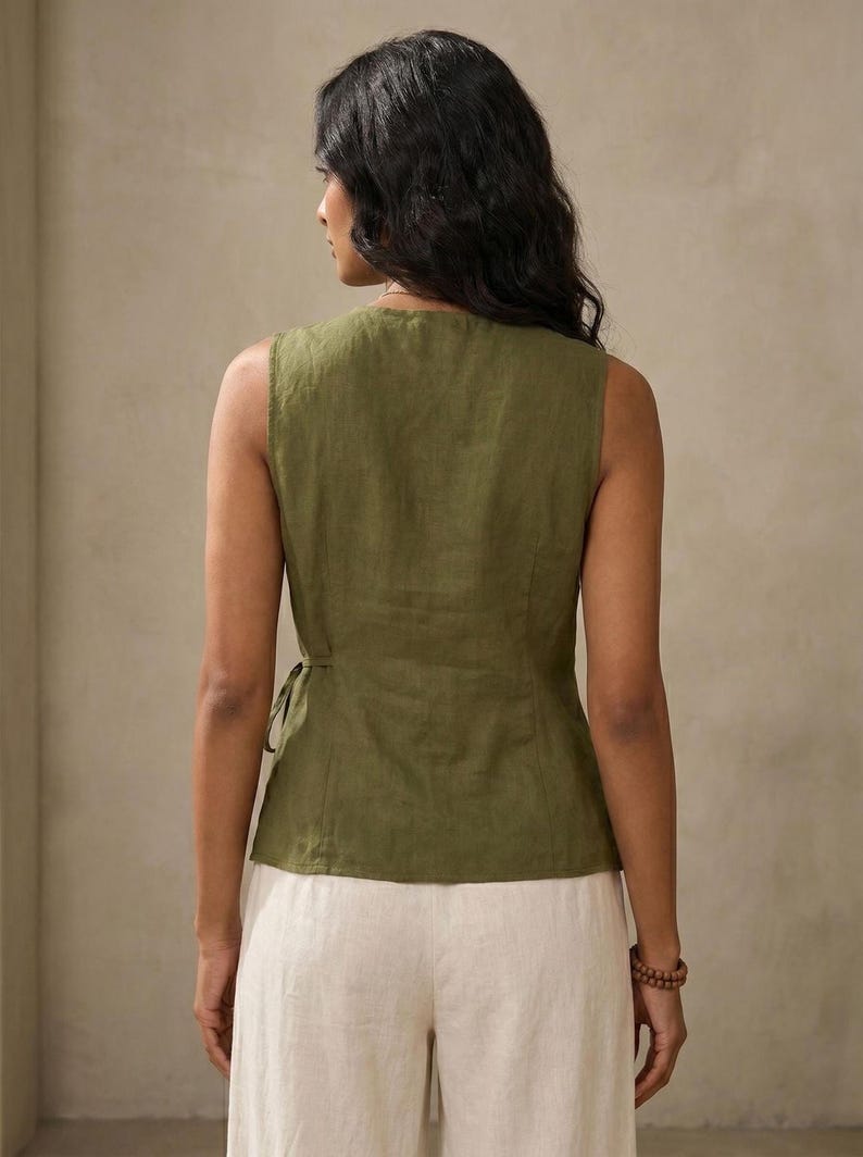 A woman wearing a green sleeveless top and white pants is facing away from the camera, with her back to the viewer.