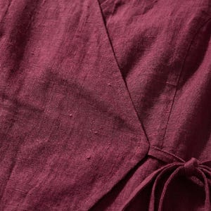 a close-up view of a burgundy-colored fabric, possibly a dress or blouse, with a tie visible at the bottom.