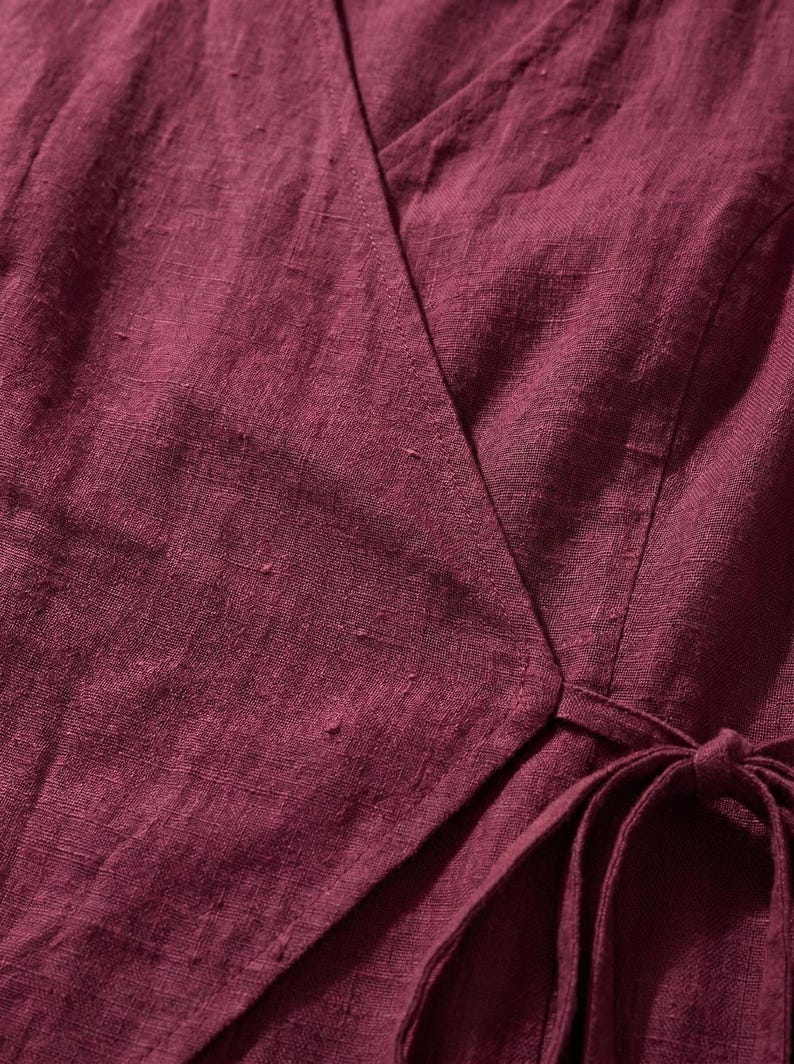a close-up view of a burgundy-colored fabric, possibly a dress or blouse, with a tie visible at the bottom.