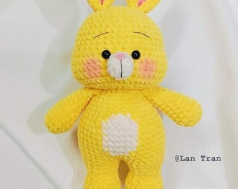 May include: A yellow crochet bunny with pink inner ears and rosy cheeks. The bunny has black eyes and a white belly patch. The image is set against a white background. The text "@Lan Tran" is in the bottom right corner.