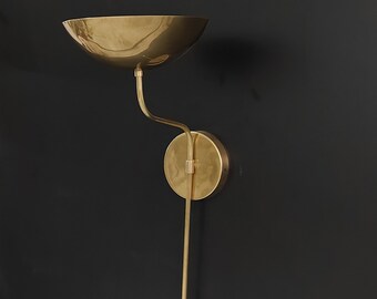 May include: A gold-toned wall sconce with a curved arm and a round, bowl-shaped shade. The sconce has a simple, modern design.