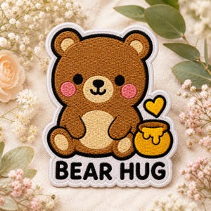 May include: An embroidered patch featuring a brown bear with a cream-colored belly, pink cheeks, and a black nose. The bear sits next to a yellow honey pot with dripping honey and a small yellow heart. The text BEAR HUG is printed in black.