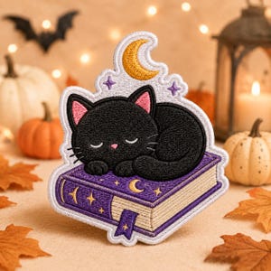 May include: An embroidered patch featuring a sleeping black cat with pink inner ears resting on a purple book. The book has gold star and crescent moon accents, a bookmark, and cream-colored pages. Above the cat is a gold crescent moon.