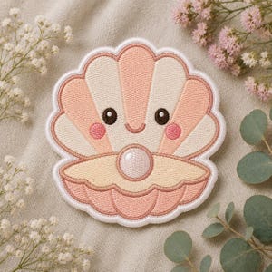 May include: An embroidered patch shaped like an open seashell with a smiling face and a pearl inside. The shell features alternating stripes of soft peach and cream thread, with small pink circles for cheeks and dark brown eyes and a mouth.