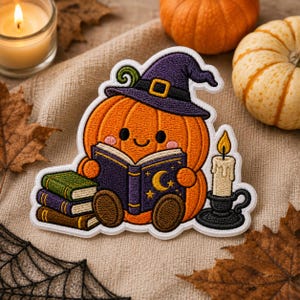 May include: An embroidered patch featuring a smiling orange pumpkin wearing a purple witch hat. The pumpkin holds an open dark purple book with a gold moon and stars. Beside it are three stacked books and a lit candle in a black holder.