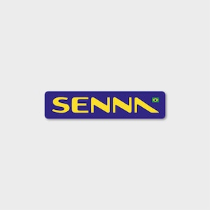 May include: A blue rectangular sticker with the word "SENNA" in yellow letters and a small Brazilian flag in the top right corner.