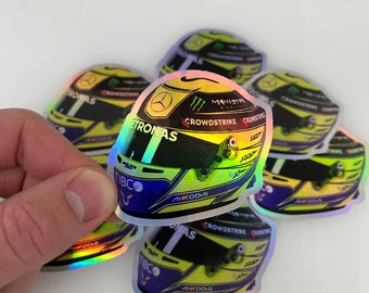 May include: A set of six holographic stickers featuring a Formula 1 driver's helmet. The helmet is yellow and black with a blue visor and various sponsors' logos, including Petronas, Monster Energy, Crowdstrike, and Tibco.